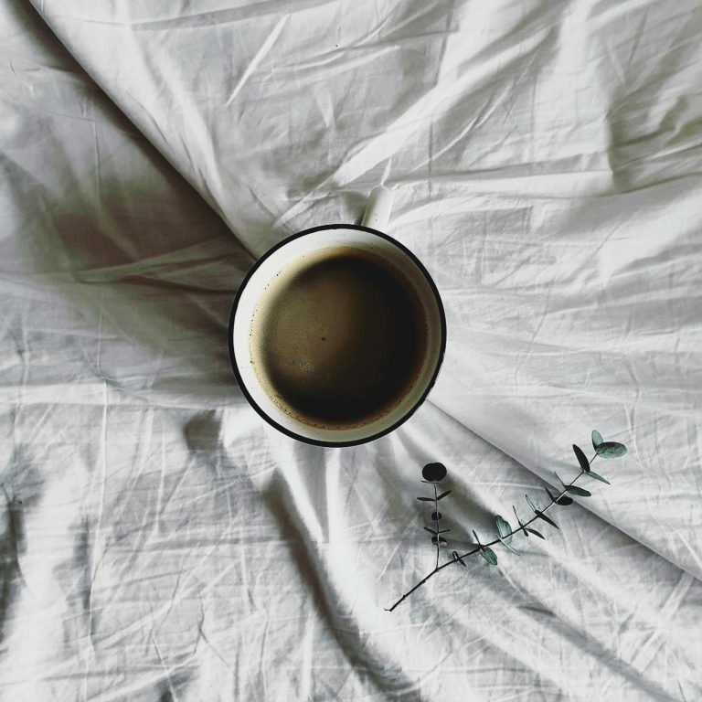 Top view of a coffee cup on crumpled white fabric with a small branch, creating a cozy atmosphere.